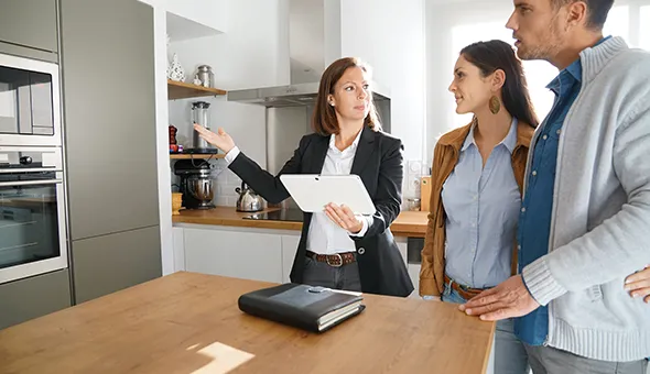 A man and woman stand in a modern kitchen, looking at a tablet, discussing plans for expanding their living space.