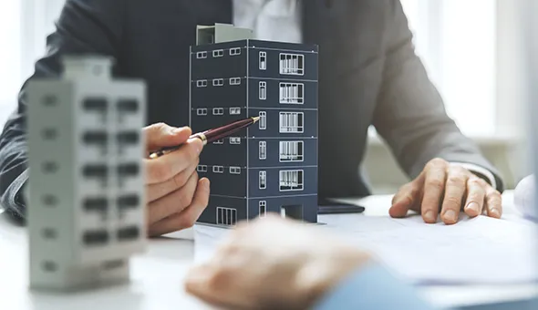 A suited man examines a building model while holding a pencil, representing property consulting for commercial expansion.
