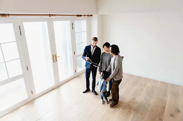A couple stands with a real estate agent in an empty room, exploring possibilities for Home Downsizing Real Estate.