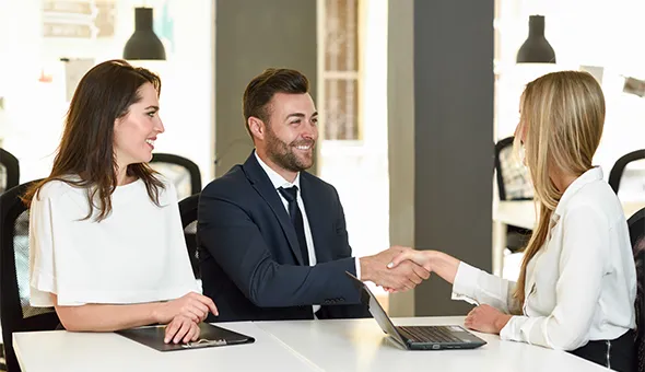 In an office setting, a man shakes hands with another women, signaling a deal related to a commercial real estate venture.